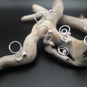 Plusieurs boucles d'oreilles en argent, faites de billes et anneaux imbriqués, présentées sur un morceau de bois flotté